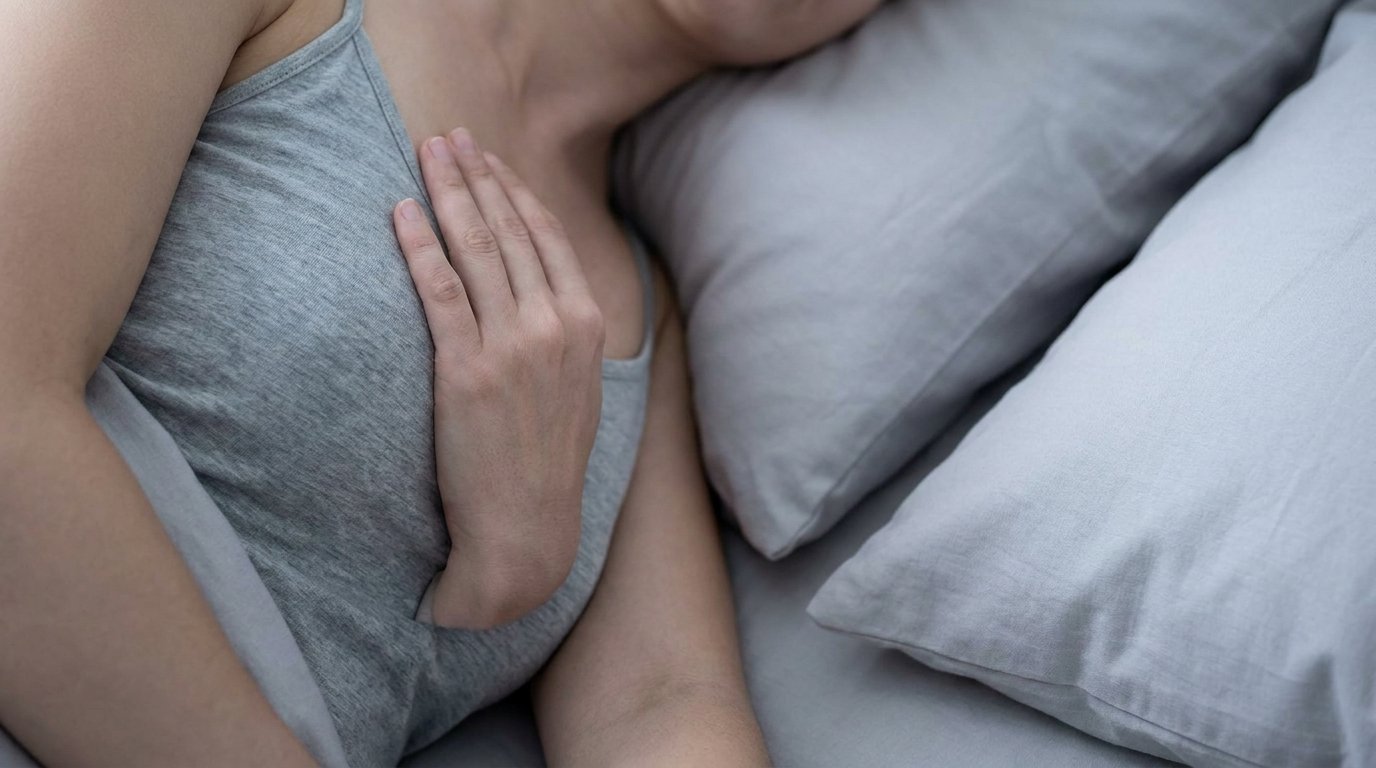 Hands pressing against the chest of a person lying on their side on a plain pillow, wearing a plain camisole.